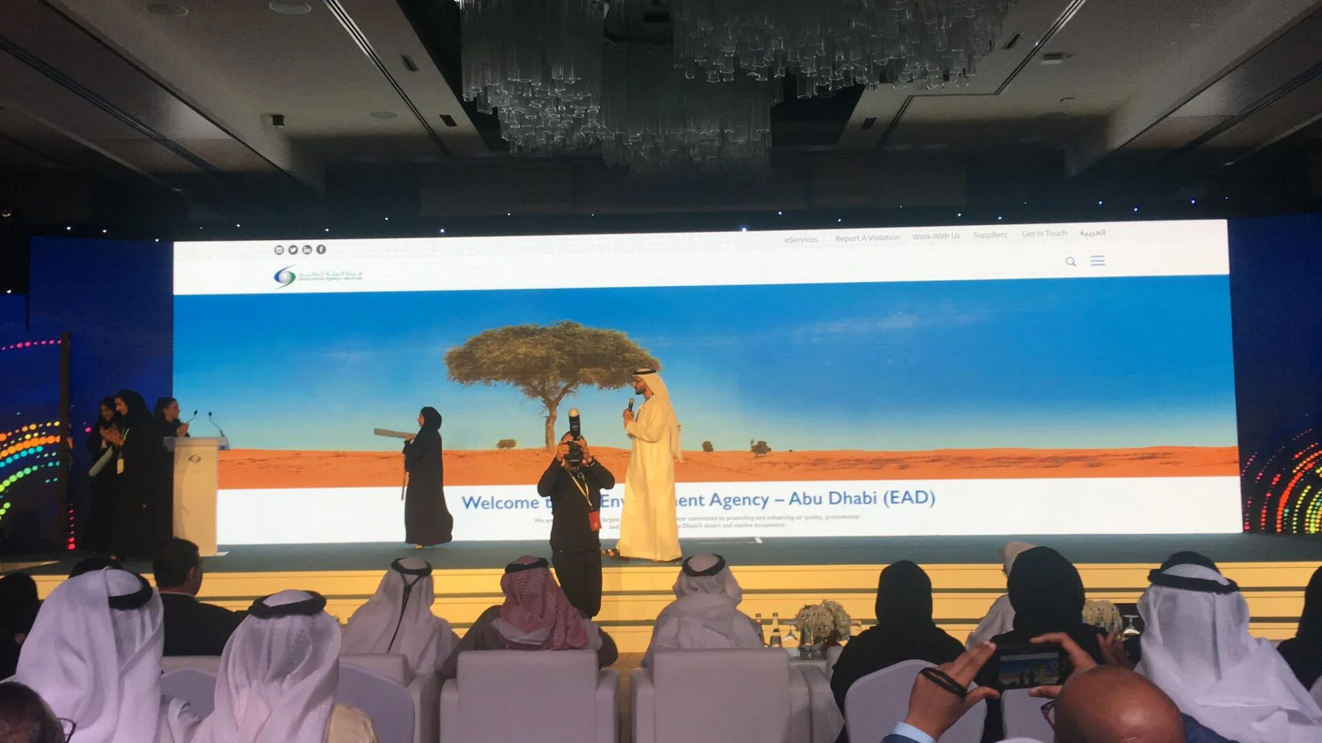 Employees holding large paintbrushes "revealing" a website on a large screen at an event.