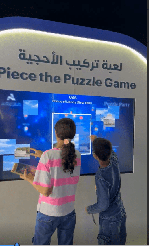Children and adult attendees solving an interactive world map puzzle game at Abu Dhabi Airports event booth.